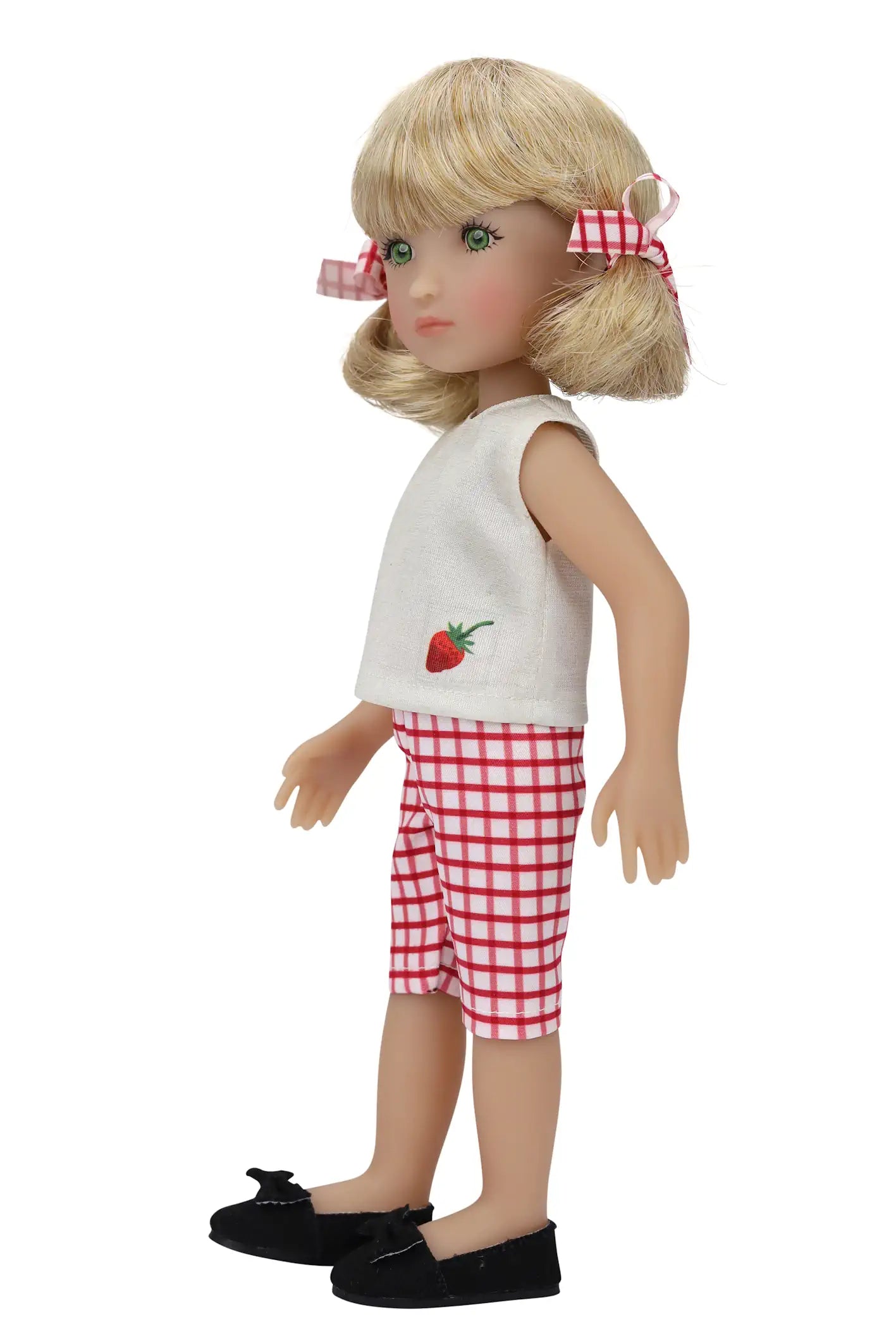 Summer, a doll with blonde pigtails and checkered bows, in a white top with strawberry embroidery and shorts,standing in a side profile.