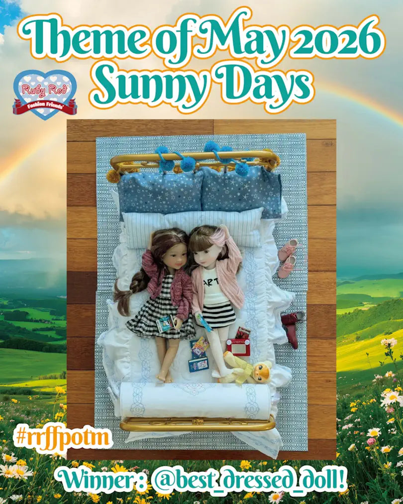 Two dolls on a bed with a scenic background and text about a theme for May 2026.