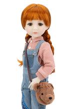 Doll with red hair styled in pigtails, wearing a pink sweater and blue overalls, holding a brown bag with a bear design.