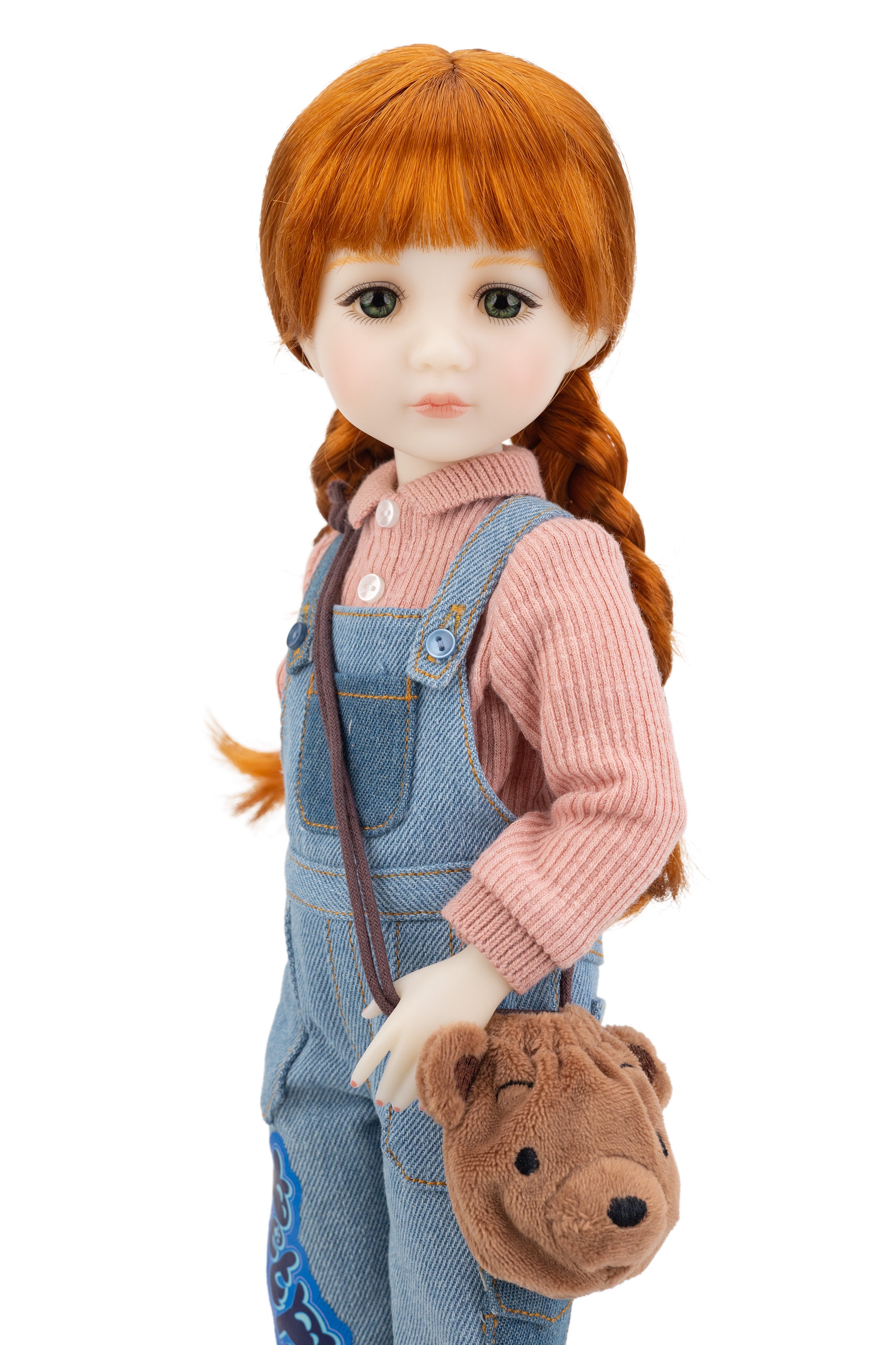 Doll with red hair styled in pigtails, wearing a pink sweater and blue overalls, holding a brown bag with a bear design.