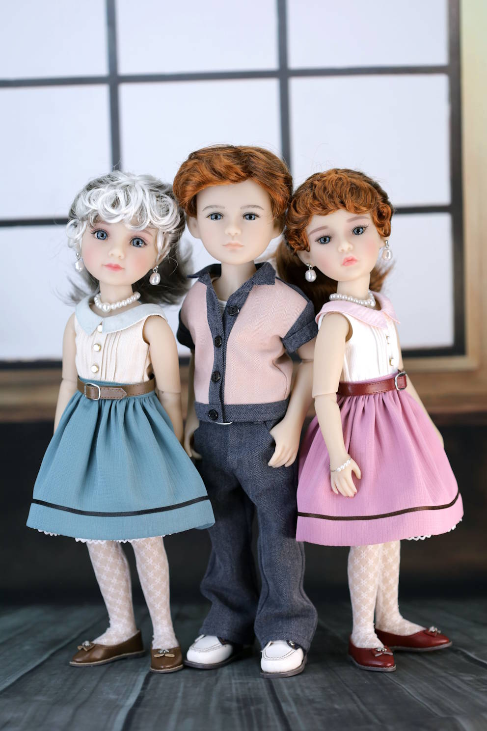 Three dolls in formal attire standing together against a neutral background