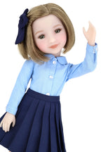 Doll wearing a blue shirt and navy skirt with a navy bow on a white background