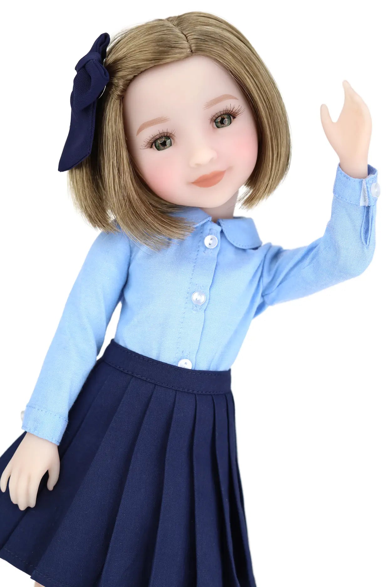 Doll wearing a blue shirt and navy skirt with a navy bow on a white background