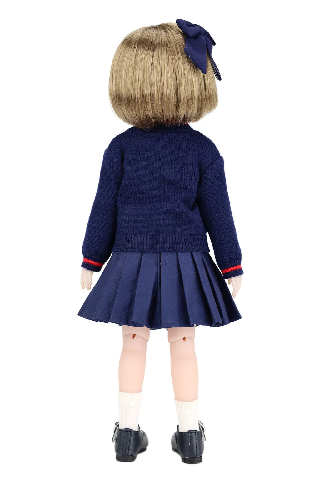 Back view of a doll wearing a navy blue outfit with a pleated skirt and bow hair accessory on a white background.
