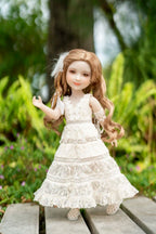 Doll in a white dress with lace details standing on a wooden surface with a natural background.