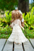 Doll in a white lace dress standing on a wooden bench with greenery in the background