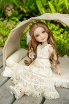 Doll in a white dress sitting under a canopy with greenery in the background