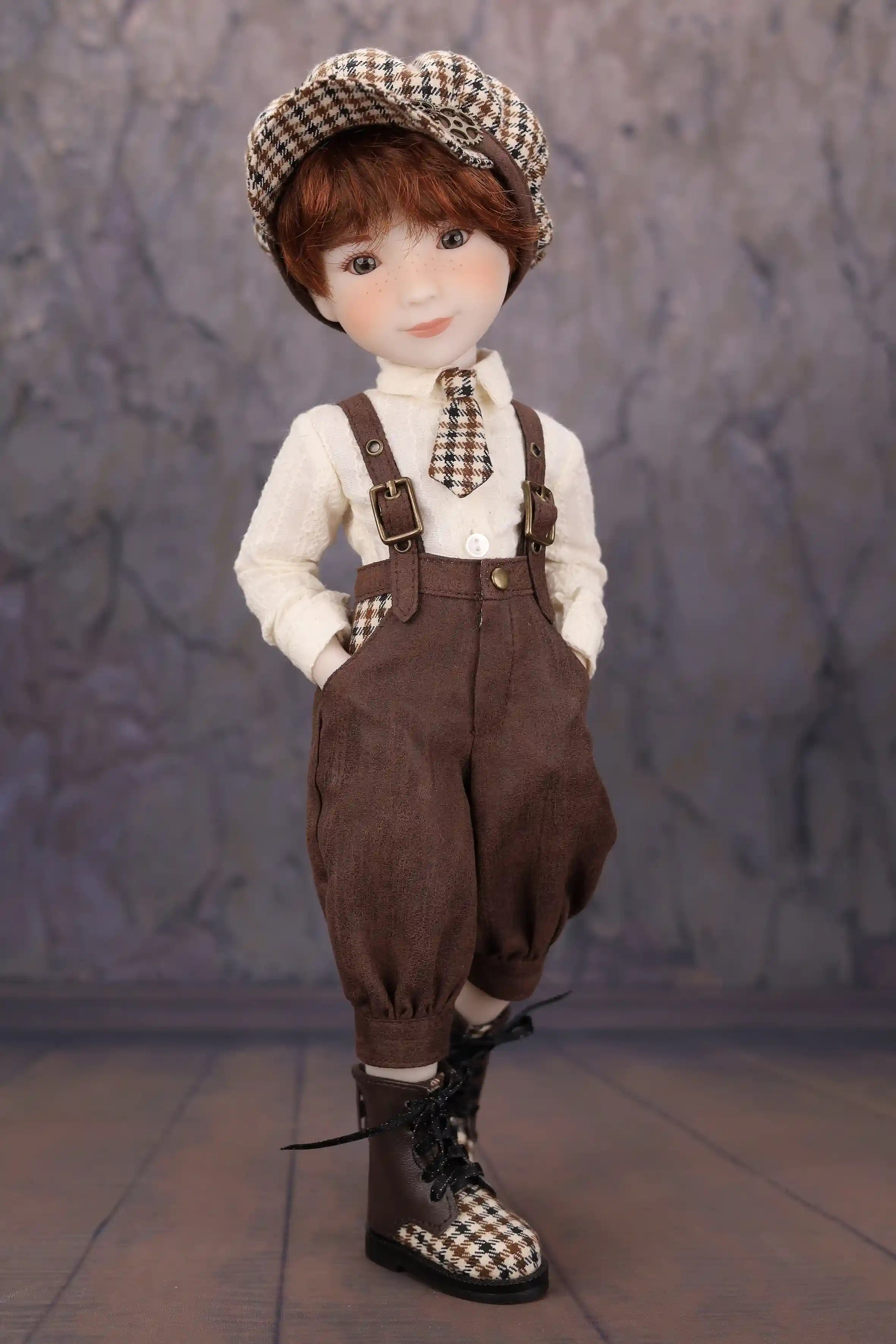 Doll wearing a checkered hat, white shirt, brown overalls, and black boots against a gray background.
