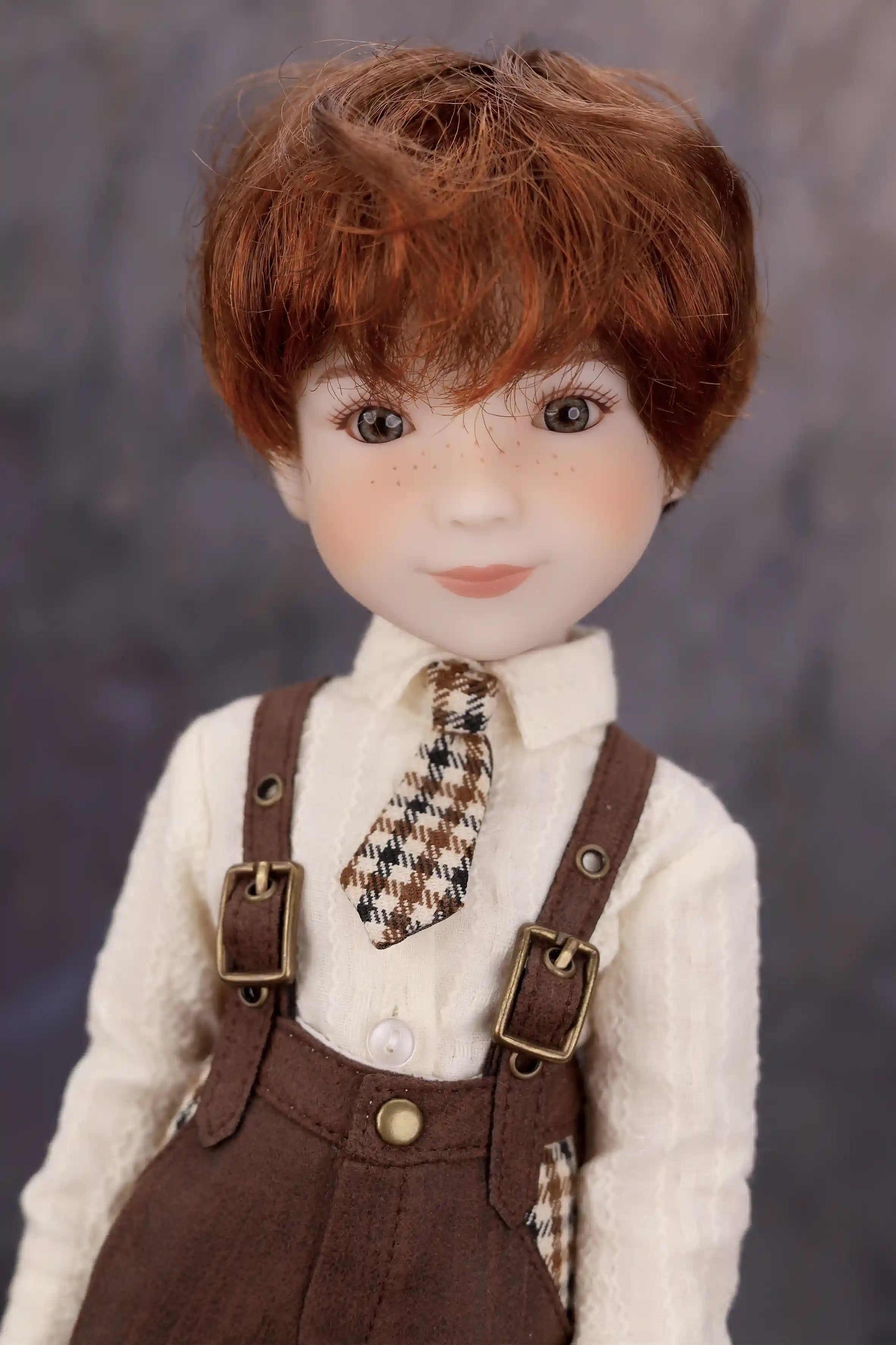 Doll with red hair wearing a white shirt, brown overalls, and a plaid tie against a dark background