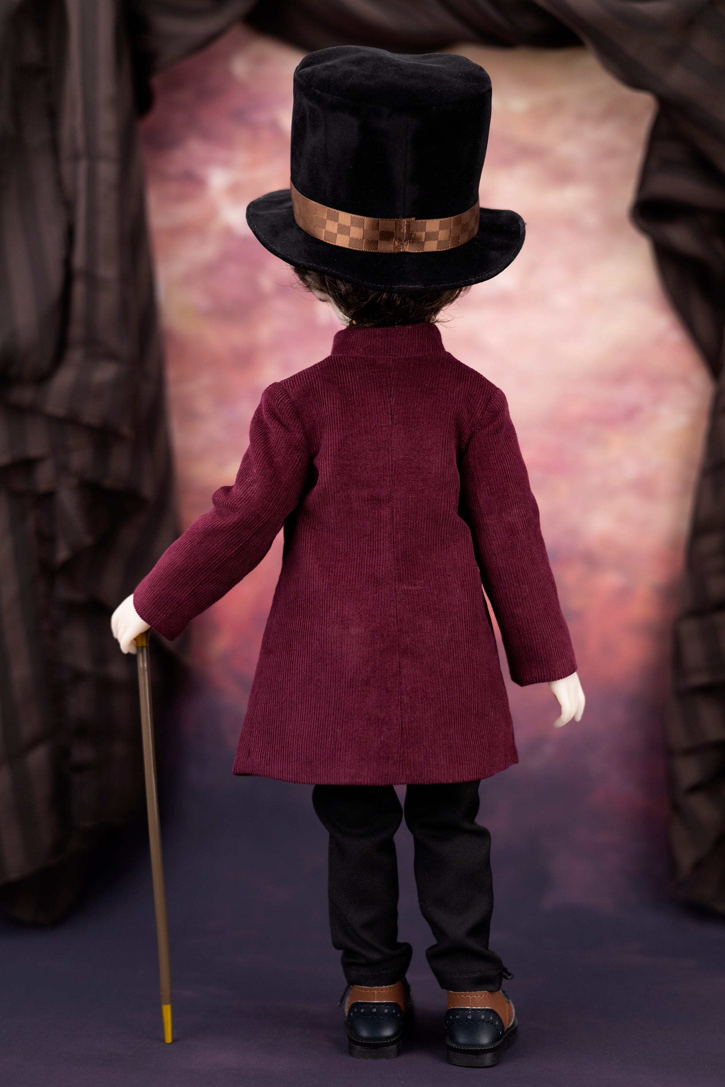 Doll in a burgundy red corduroy coat and black top hat with a cane, standing against a textured purple background.
