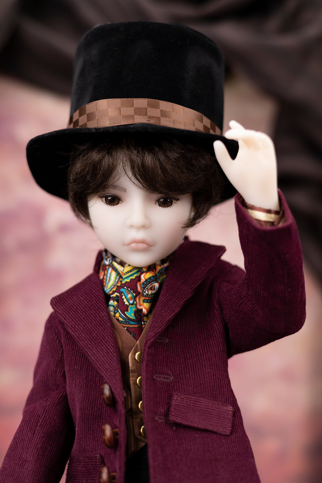 Doll wearing a black hat and  burgundy red corduroy coat with a blurred background