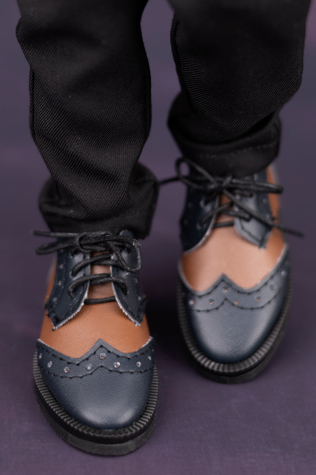 Black leather doll shoes with brogue details worn with black pants on a dark background
