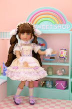 Doll in a pastel outfit standing in front of a 'Sweet Shop' display.