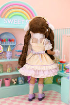Doll in a yellow dress standing in front of a pastel-colored candy store display.