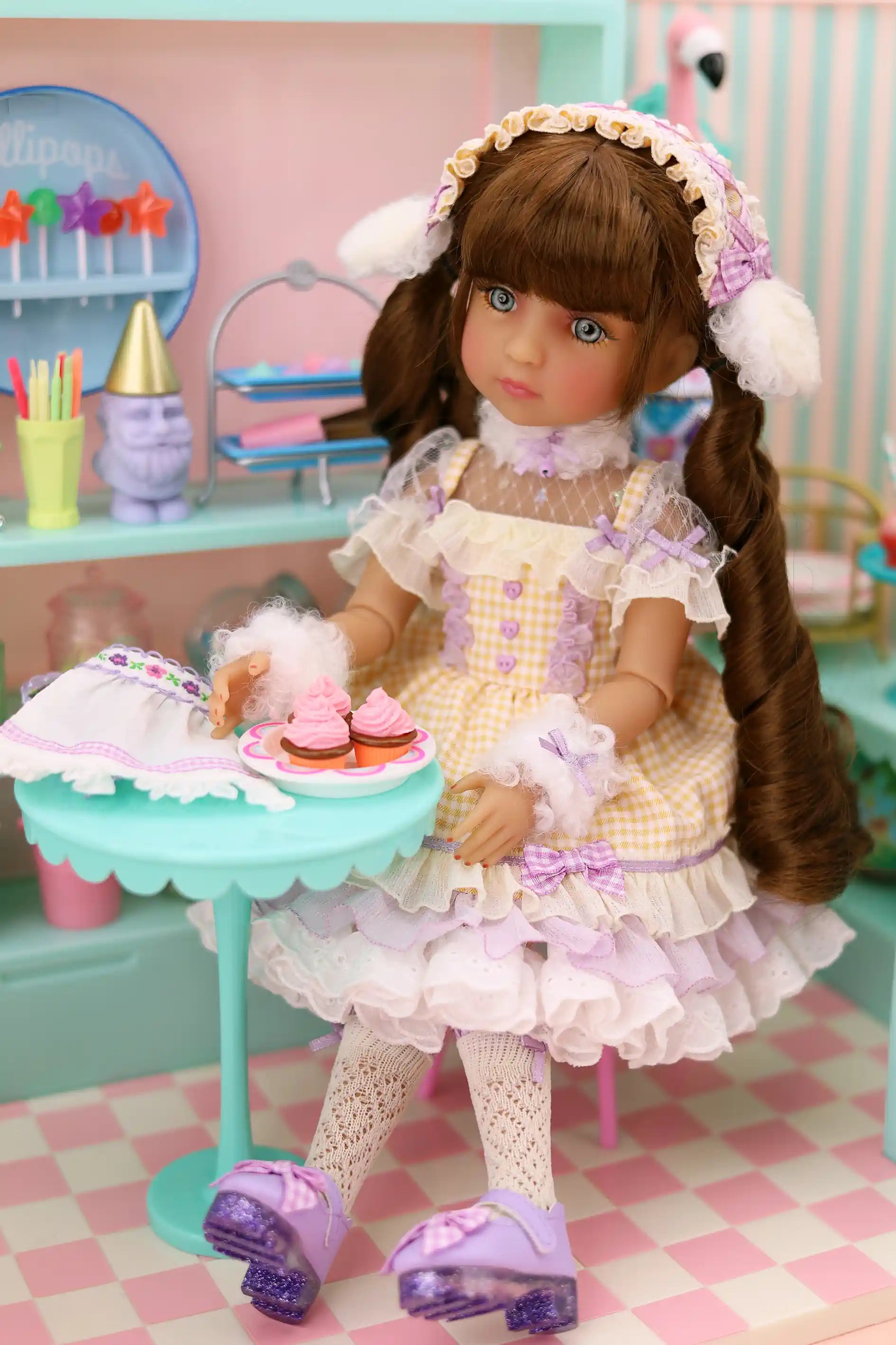Doll in a pastel dress with a cake stand and cupcakes in a playroom setting