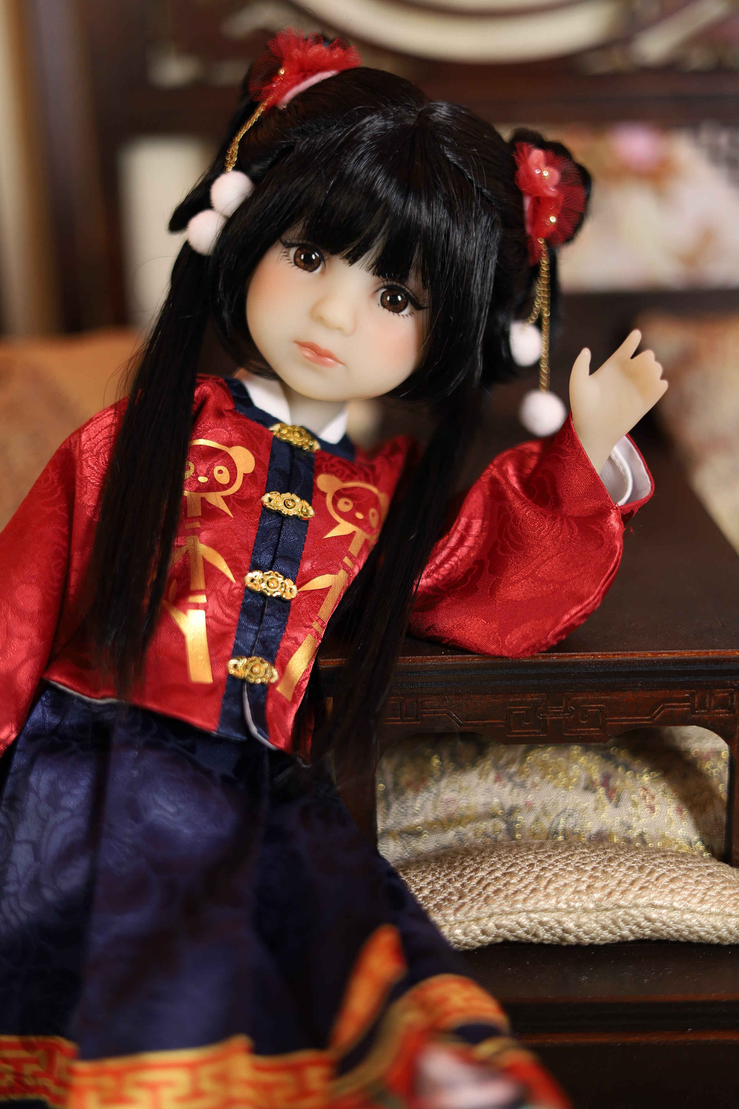 Doll in traditional Chinese red and blue outfit with decorative hair accessories on a wooden surface.