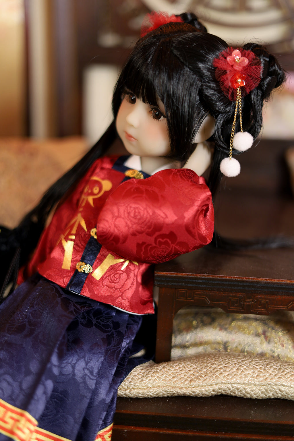 Traditional doll in red and blue outfit with floral hair accessories on a wooden surface.