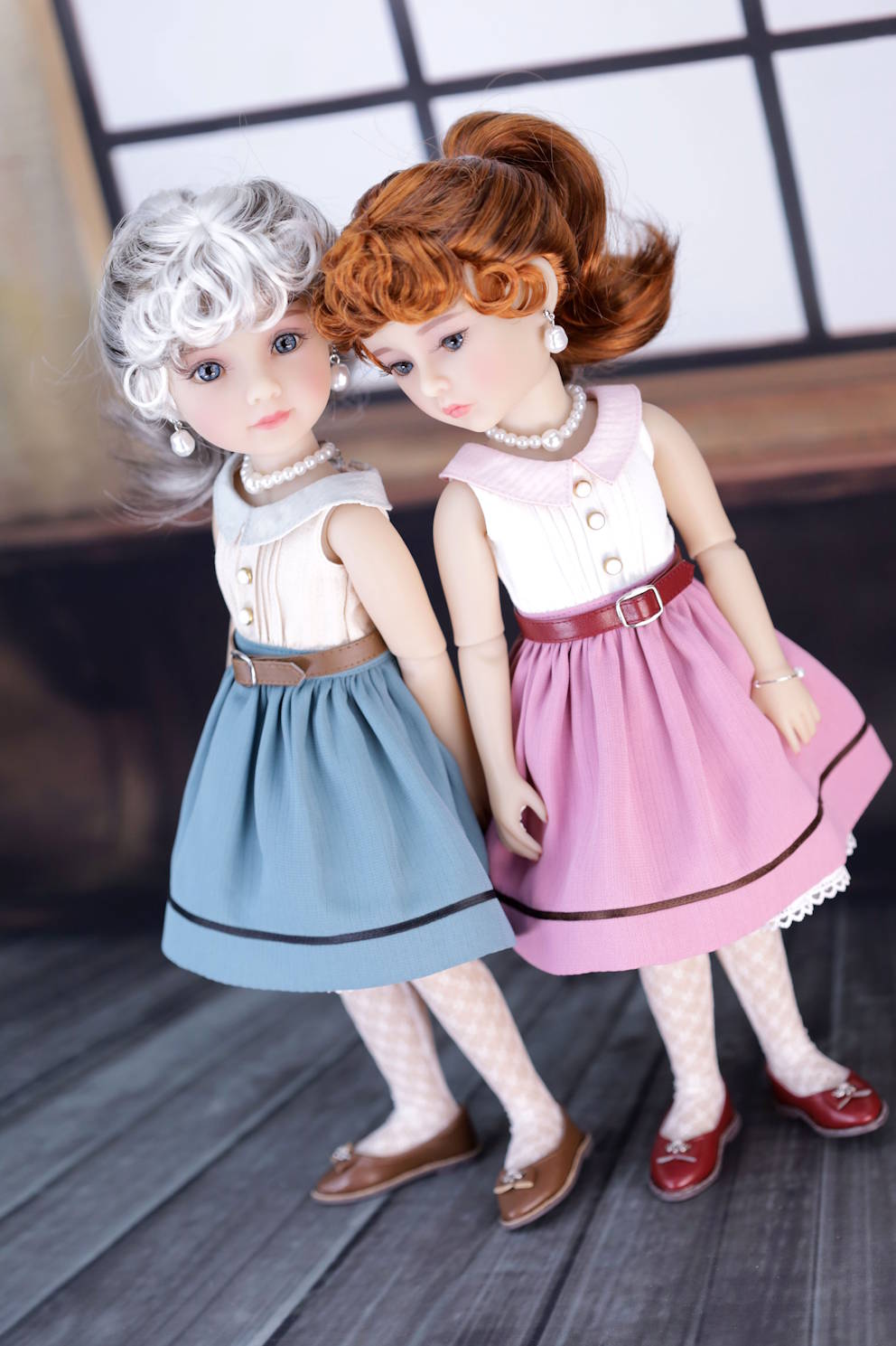 Two dolls with styled hair and outfits standing on a wooden floor.