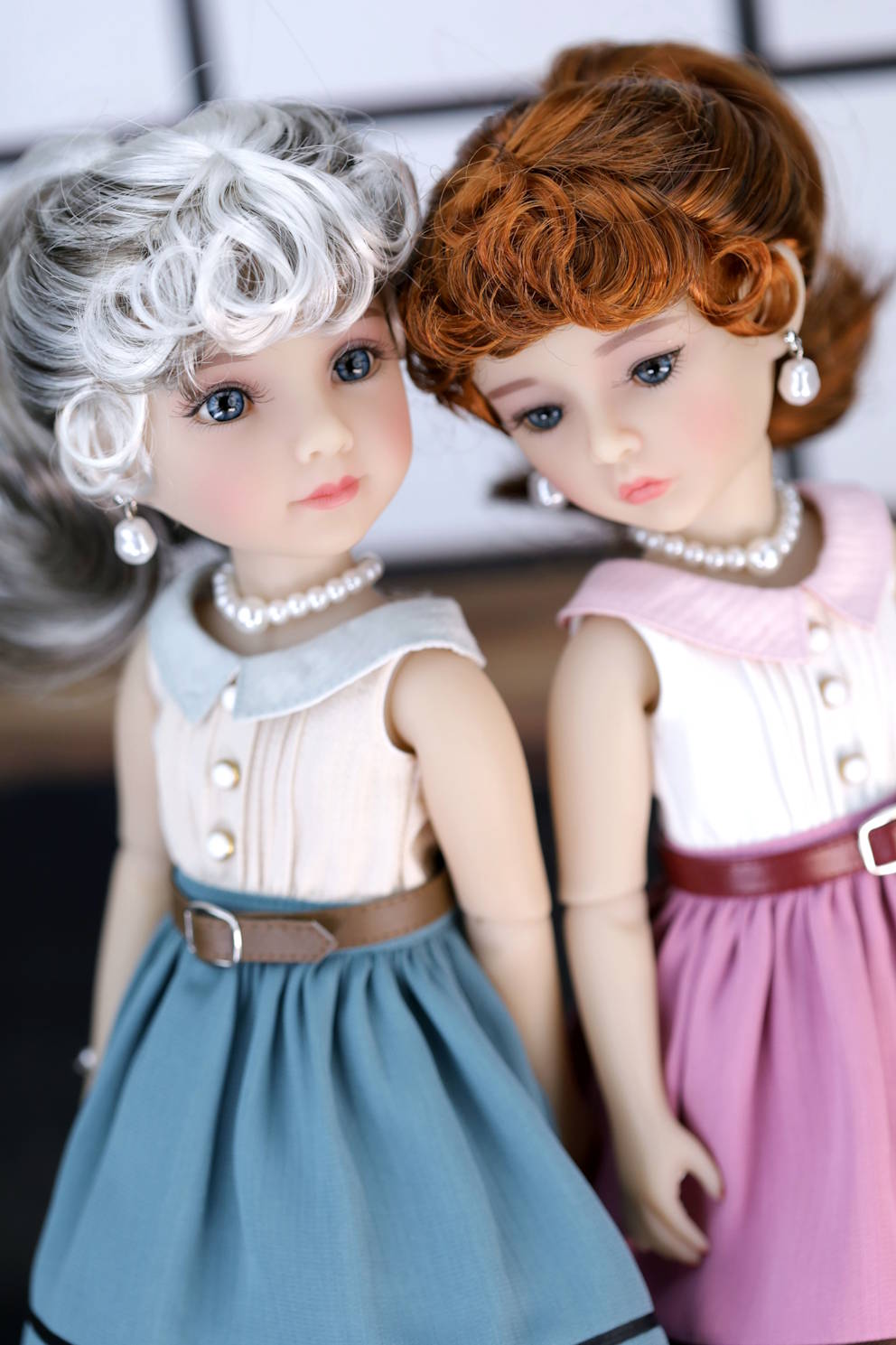 Two dolls with styled hair and dresses against a neutral background