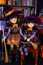 Two dolls in Halloween-themed outfits with brooms in a room with bookshelves.
