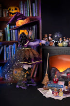 Halloween-themed doll in a witch costume with a fireplace and bookshelf in the background.