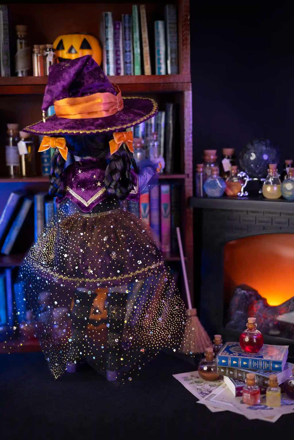 Doll witch figure with a broom and pumpkin hat in a cozy room with books and potions.