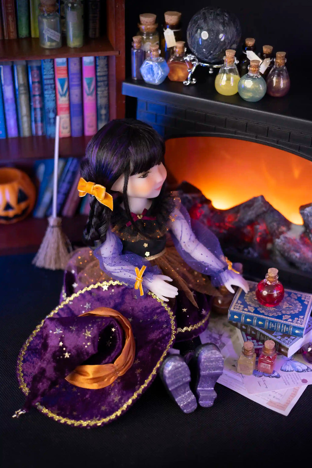 Doll figurine with a purple hat and broom in front of a fireplace with Halloween decorations.