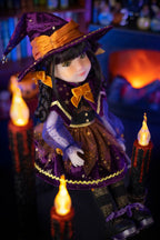 Doll dressed as a witch with a purple hat and outfit, surrounded by candles in a cozy, dimly lit room.