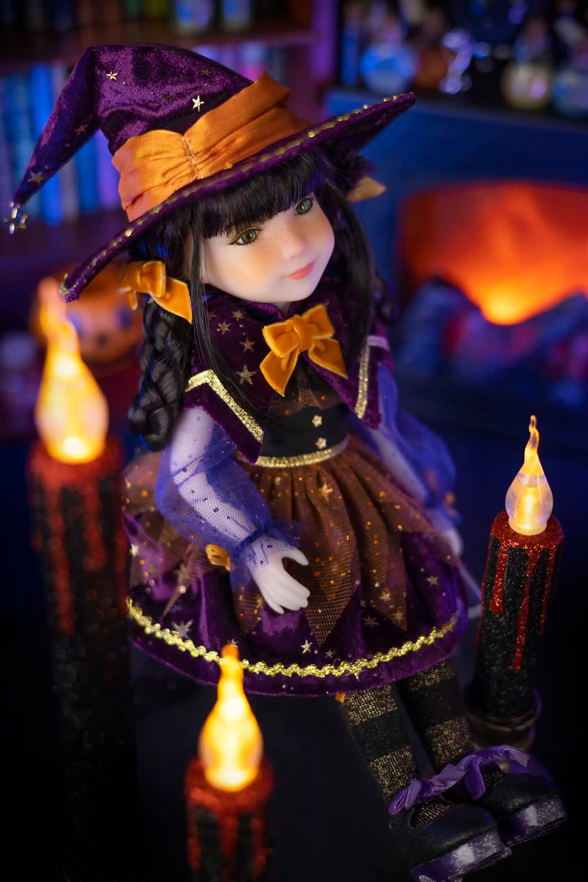 Doll dressed as a witch with a purple hat and outfit, surrounded by candles in a cozy, dimly lit room.